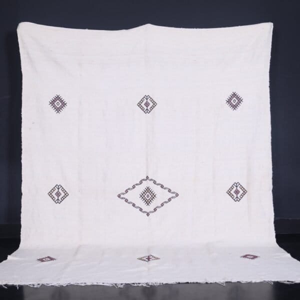 Moroccan man holding or standing near a white 6.2 x 9.2 FT flat woven Berber kilim rug