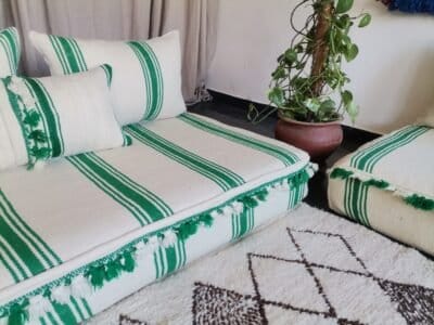 Left side of Moroccan wool couch in cream with green stripes and pom-pom edges – playful handcrafted floor seating