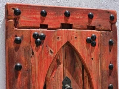 Upper section of red Moroccan wood panel showing iron studs and arched construction