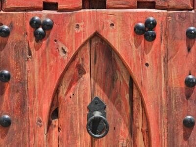 Rustic Moroccan panel featuring arched design with centered iron knocker on red wood