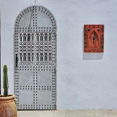 Red vintage Moroccan wooden panel hung on white wall next to traditional arched metal door with cactus pot
