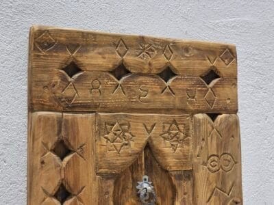 Upper part of handcrafted Moroccan wooden panel featuring geometric Berber carvings and rustic wood finish