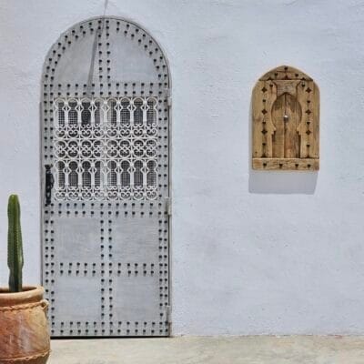 Moroccan panel mounted on white wall next to arched traditional door and cactus