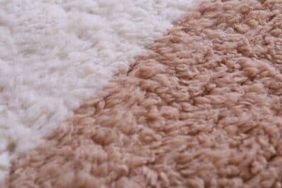 Macro zoom of wool texture on ivory and tan Moroccan rug, displaying natural fiber detail and luxurious density.